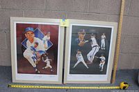 Two framed numbered prints side by side against a block wall, with tape measure for size reference, showing overall condition and scale.