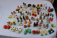 Top view photo showing over 35 vintage salt and pepper shaker sets arranged on a white cloth. Diverse designs visible including animals, vegetables, fruits, and characters, primarily ceramic or porcelain.