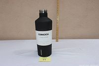 Full view of the Corkcicle 60 oz black matte canteen placed against a beige wall with a ruler behind it for scale, showing its height approximately 13 inches.