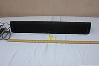 Front view of Auvio black sound bar with cables placed next to a ruler for size reference.