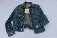 Full view of True Religion child's denim jacket laid flat, showing front side, buttons, pockets, and sleeves.