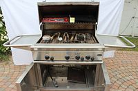 Front view of DCS stainless steel gas grill with lid open and utensils displayed