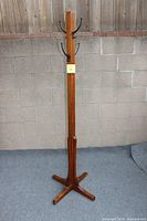 Full height view of the tall wooden coat rack with four metal hooks on each side near the top and a solid base.