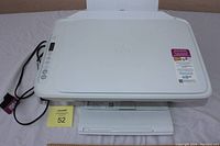 Top view of the HP Desktop 2700e all-in-one printer showing control buttons, paper input and output trays, and power cord.