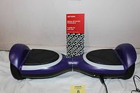 Purple Jetson Sphere All-Terrain Hoverboard with black foot pads and white trim with instruction booklet behind it, displayed against white background.