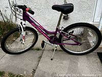 Side view of the pink and purple kids bike showing the frame, tires, seat, pedals, and kickstand.