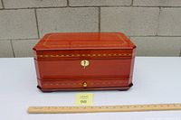 Closed mahogany jewelry box with polished finish and decorative inlaid design on lid edges, ruler in front for size reference.