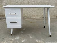 Side view of the white mid century modern style desk showing two drawers and tapered legs.