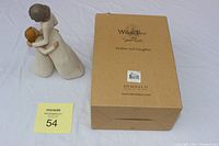 Full view of the mother and daughter figurine with the original box placed beside it on a white cloth background.