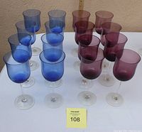 Set of 16 wine glasses, 8 blue and 8 purple, arranged on white surface with measuring ruler in background.