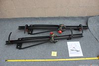 Wide shot of the Yakima bike rack on a grey carpet surface with a yellow measuring tape and a paper showing a bike mounted on a similar rack.