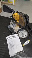 Photo of Canwood compound miter saw on floor with instruction manual and extra saw blade.