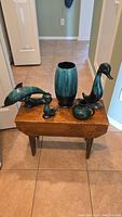 Full view of the five Blue Mountain Pottery items on a wooden table showing dolphin, large duck, small duck, vase, and small picture/plaque.