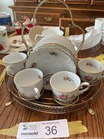 Set of four vintage china cocoa cups with matching saucers set inside a brass carrier on a wooden surface.