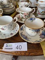 Close-up showing pairs of teacups and saucers with distinct floral patterns and gold rims.