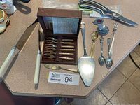 Photo of assorted cutlery including the boxed set of bronze appetizer forks, large cake cutter, souvenir butter spreader, and kitchen shears on a kitchen counter.
