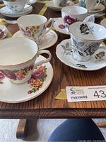 Photo showing six assorted floral motif teacups on matching saucers arranged on a wooden table. Displays variety of designs and colors with gold trim on porcelain.