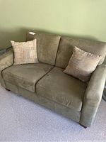 Front view of sage green love seat with cushions and two throw pillows.