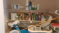 Cleaning and laundry supplies organized on shelving above washer and dryer, showing laundry baskets, mop bucket, mop, and assorted cleaning products