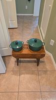Two green enameled Dutch ovens and a steamer insert on wooden bench