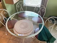 Patio table with glass top, four chairs with vinyl seats, green table cloth, and wicker placemats visible from side angle by window