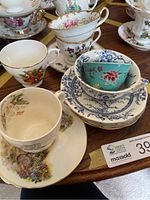 Photo showing multiple stacked china cups and saucers with floral patterns on wooden table
