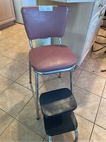 Front view of the vintage Morris chair with padded seat and backrest and attached black two-step stool.