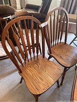 Two oak dining chairs side by side showing full front view of seats and backrests.
