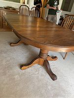Angled side view of the oak dining table showing wood grain and curved legs of pedestal base