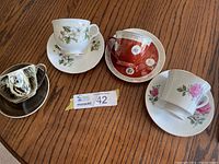 Four assorted teacups with matching saucers displayed on wooden table.