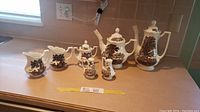 Overall view of all 7 pieces on counter showing coffee pot, tea pot, two creamers, sugar bowl, salt and pepper shakers in brown and white porcelain