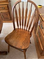 Side angle view of one oak dining chair showing curved backrest with vertical slats and contoured seat with oak grain.