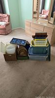 Multiple storage bins stacked showing variety including woven baskets, clear plastic bins, blue folding totes, and plastic trays