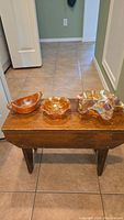 Three vintage carnival glass candy dishes on a wooden bench, showing varying shapes and iridescent orange-gold color.