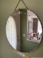 Full front view of vintage round beveled edge mirror showing floral etching and chain against a wall.