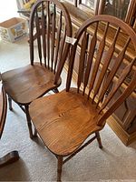 Pair of vintage oak dining chairs seen from front showing contoured wood seats, turned legs, and curved spindle backs.