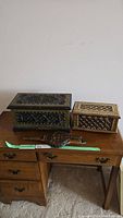 Two antique African decorative strong boxes and a vintage Lourdes bellows displayed on a wooden desk.