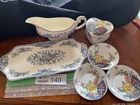 Photo showing Myott Son & Co blue floral gravy boat, Crown Ducal Bristol cake plate, and Mann tobacco leaf design heart-shaped trinket dish with small plates.