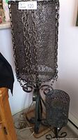 Floor lamp with black metal mesh shade and chain accents, showing height and metal base with scroll design.