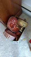 Box of copper cake molds and brass bowl on elephants on carpeted floor