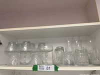 Wide view of crystal and glass drinkware assortment on shelf showing various stemmed glasses, tumblers, and cut glass cups