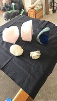 Five mineral specimens placed on a black cloth: two pink rose quartz cuts, blue agate slice, coral piece, and rough quartz piece.