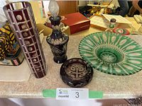 Full set of four cut to clear glassware pieces on a countertop including red tall vase, black decanter with stopper, red ashtray, green dish