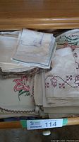 Drawer filled with assorted embroidered linens, napkins, and small table coverings, showing a variety of colors and designs including floral embroidery and scalloped edges.