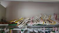 Shelf filled with numerous plastic hangers in white, yellow, and pink, tightly stacked.