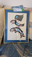Full view of the framed Indigenous art showing the eagle and salmon design, with blue matting and gold frame.
