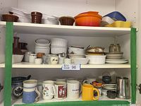 Shelf with mixed kitchenware items including mugs, bowls, ramekins, small plates, casseroles, and pottery pieces in varied colors and materials.