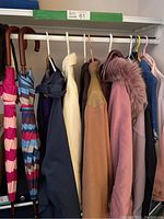 Photo showing variety of jackets, coats, sweaters hanging on a rack with umbrellas on the side.