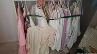 Photo showing a row of assorted large size ladies tops hanging on a green strap on a clothing rack, including light colored and patterned items.