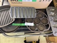 Photo showing the full set of cast iron pans including corncob pan, fish pan, muffin pan, and grill pan stacked and displayed together.